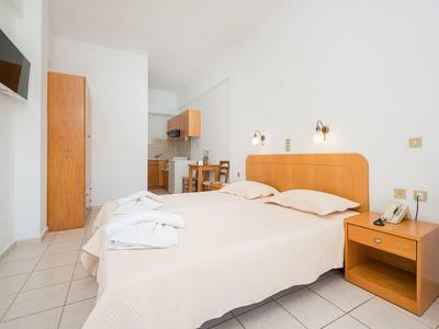 Hell eingerichtetes Schlafzimmer mit Doppelbett, Holzmöbeln und hellen Fliesen auf dem Boden.
