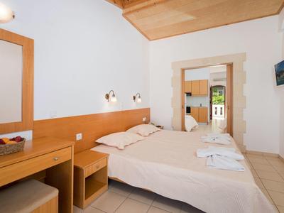 Helles Schlafzimmer mit Doppelbett, Holzdecke, Schreibtisch, Korb mit Obst und kleinem Wandfernseher.