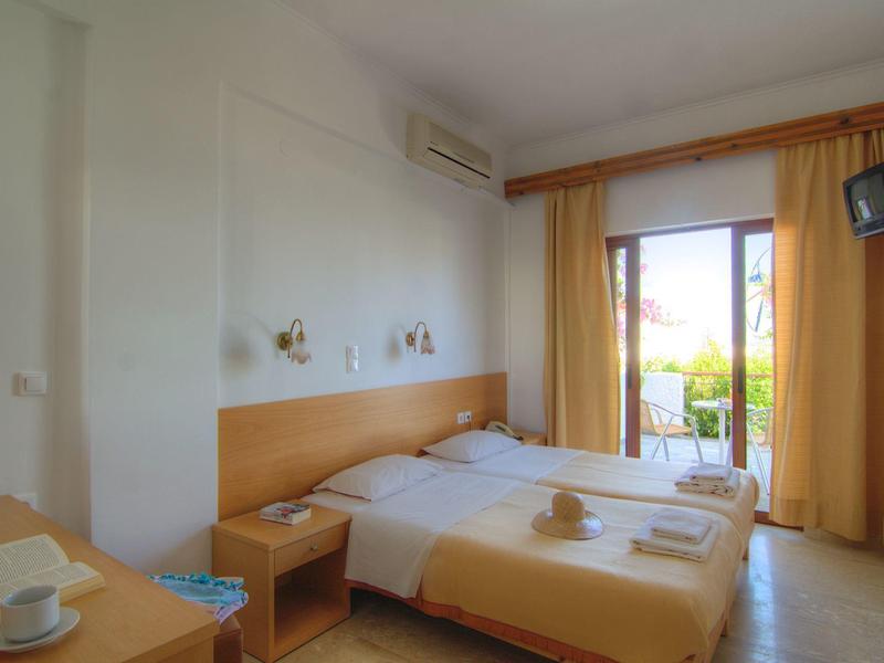 Habitación de hotel luminosa con dos camas individuales, mesita de noche y balcón con vista al exterior.