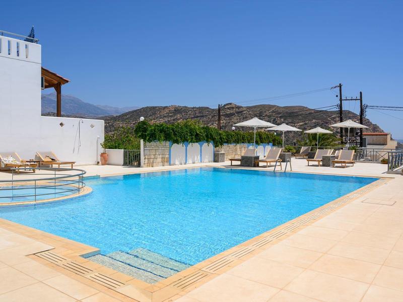 Una gran piscina al aire libre con tumbonas y vista a montañas y mar bajo un cielo despejado.