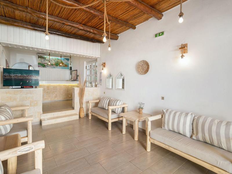 Sala de espera luminosa de hotel con muebles de madera, cojines a rayas y decoración natural.