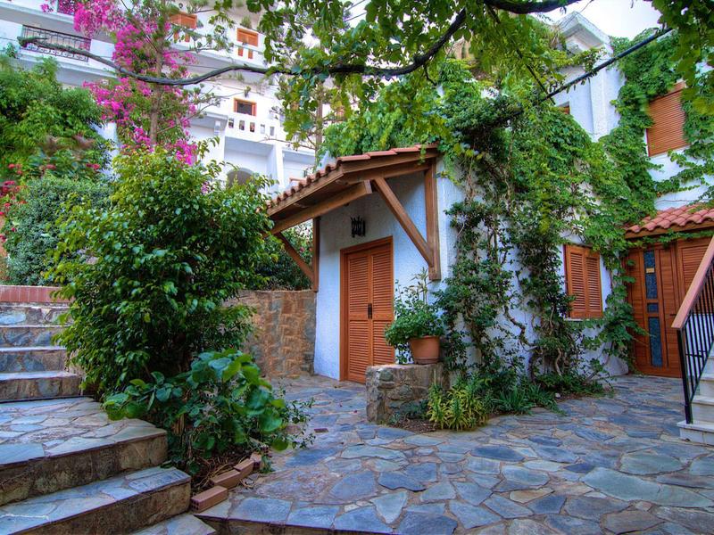 Un encantador patio con baldosas de piedra, abundante vegetación y edificios blancos con puertas de madera.