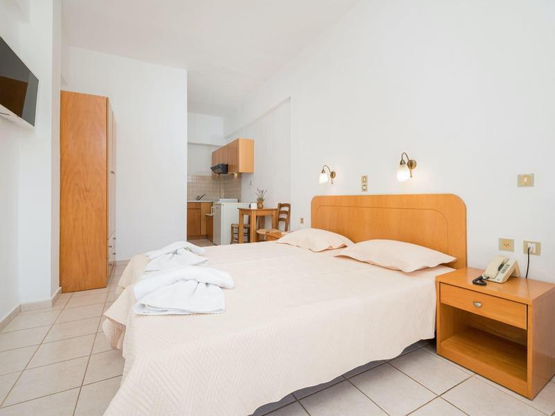 Habitación de hotel luminosa con dos camas, mesita de noche, televisor y pequeña mesa de comedor al fondo.