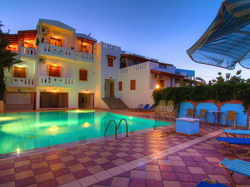 Piscina iluminada junto a un edificio de hotel al atardecer con hamacas y sombra