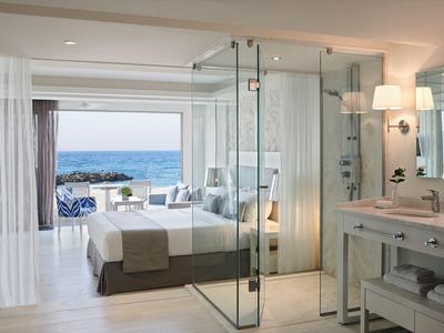 Modernes Hotelzimmer mit Meerblick, großem Bett und Glasdusche neben dem Badezimmer