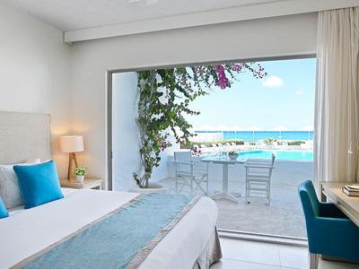 Camera d'hotel luminosa con letto e vista mare tramite ampia porta scorrevole verso terrazza con sedie.