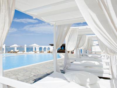 Área de piscina de lujo con cortinas blancas y vista al mar bajo un cielo azul.