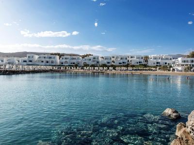 Costa con agua cristalina y edificios blancos bajo un cielo azul.