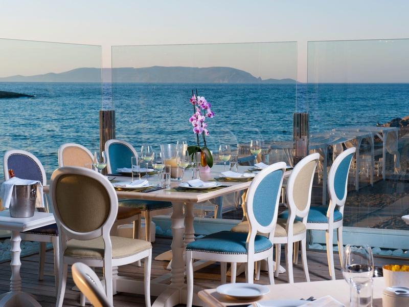 Restaurantterrasse mit blauen Stühlen und Meerblick unter klarem Himmel am späten Nachmittag.