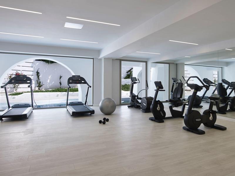 Moderner Fitnessraum mit großen Fenstern, Laufbändern, Fahrradergometern und Gymnastikball.