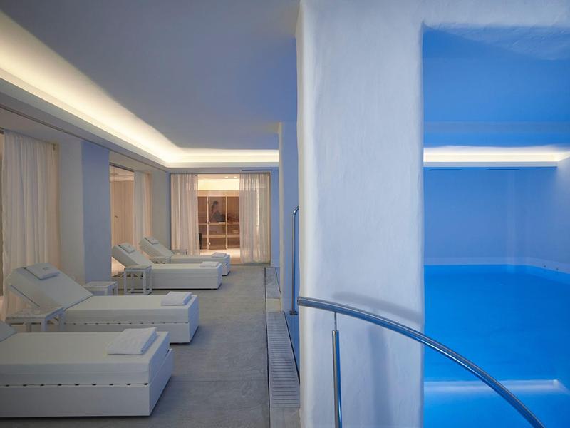 Moderner Innenpool mit strahlend blauem Wasser und weißen Liegen auf grauem Boden.