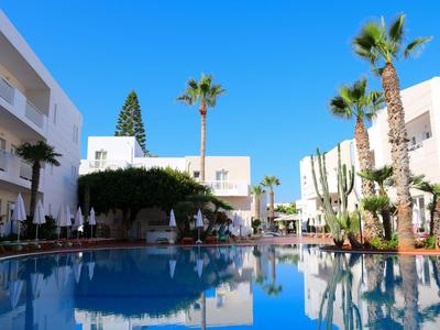 Piscina moderna dell'hotel con palme e edifici bianchi sotto un cielo azzurro limpido.