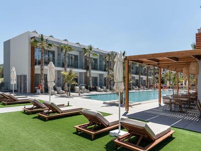 Area piscina moderna dell'hotel con lettini, ombrelloni e edificio a più piani sullo sfondo.