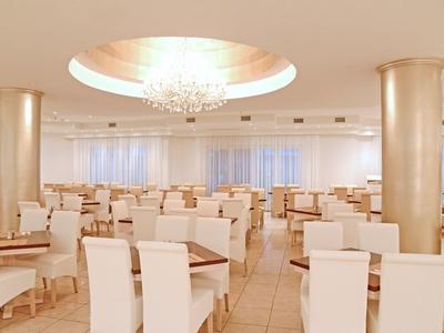 Ristorante spazioso e luminoso con sedie bianche, tavoli e lampadario al soffitto.