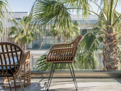 Sedie da giardino moderne su una terrazza con palme e parapetto in vetro alla luce del sole.