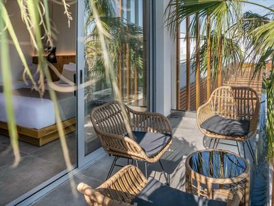 Balcone con tre sedie e tavolo, vista su una camera d'hotel con letto e pianta.