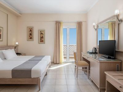 Camera d'hotel luminosa con letto matrimoniale, scrivania, TV e balcone con vista mare.