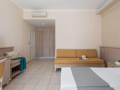 Camera d'hotel semplice con letto, divano, TV e scrivania in tonalità neutre.