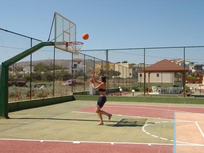 Donna che gioca a basket su un campo esterno con cielo limpido e edifici circostanti.