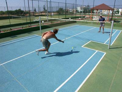Due uomini giocano a badminton su un campo all'aperto con recinzione e edifici sullo sfondo.