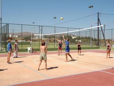 Diverse persone giocano a pallavolo su un campo esterno soleggiato con una rete pieghevole.