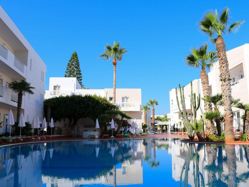 Piscina dell'hotel con palme e cielo blu, circondata da edifici bianchi.
