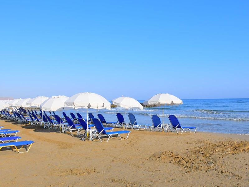 Fila di lettini blu e ombrelloni bianchi sulla spiaggia sabbiosa sotto un cielo sereno.