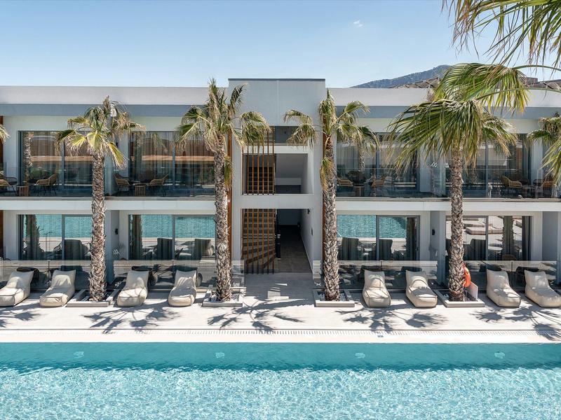 Hotel moderno con piscina, sdraio e palme sotto un cielo limpido.