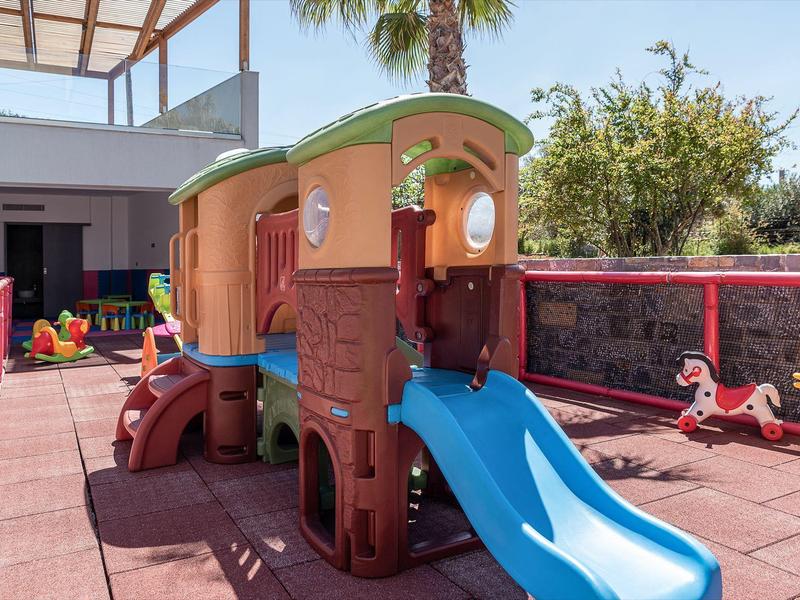 Area giochi per bambini con casetta colorata e scivolo nell'area esterna di un hotel.