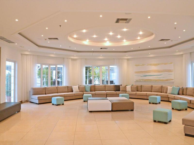 Area lobby moderna e luminosa con grandi divani, pouf e illuminazione minimalista a soffitto.
