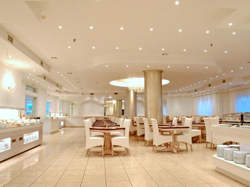 Ampia sala da pranzo dell'hotel luminosa con tavoli e sedie moderne, grande pilastro e illuminazione indiretta.