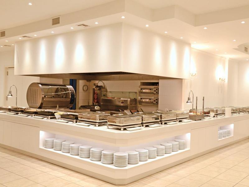 Cucina d'hotel moderna e minimalista con superfici bianche e illuminazione integrata.