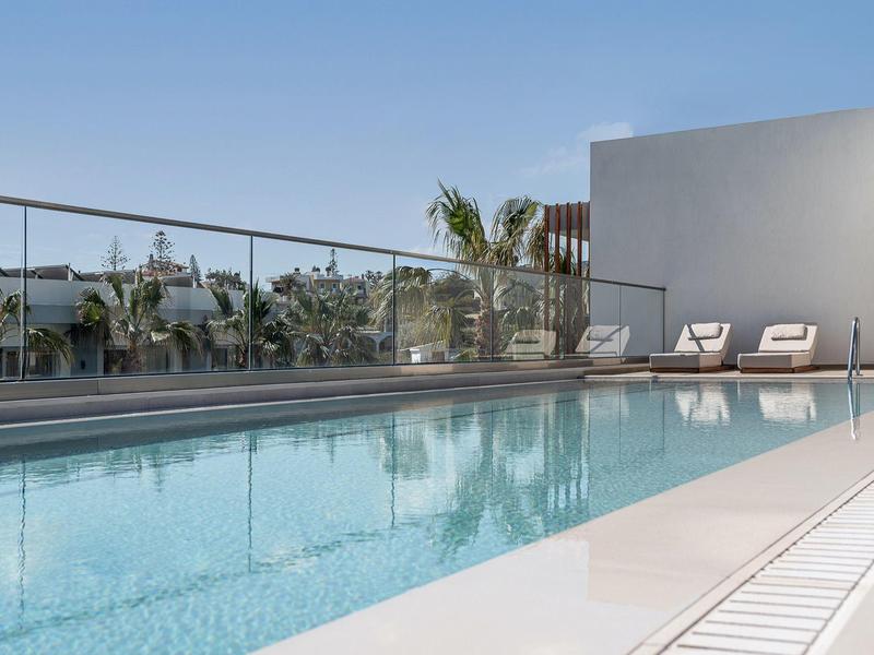 Piscina moderna con superficie d'acqua limpida e lettini sotto un cielo sereno.