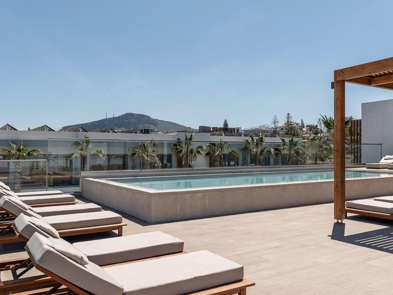 Piscina esterna moderna su una terrazza soleggiata con lettini e vista sulle montagne.