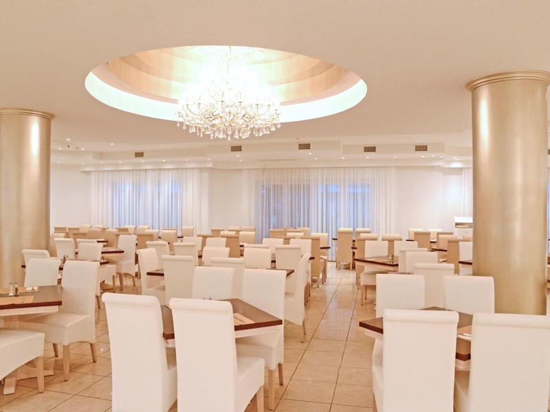 Ristorante spazioso e luminoso con sedie bianche, tavoli e lampadario al soffitto.