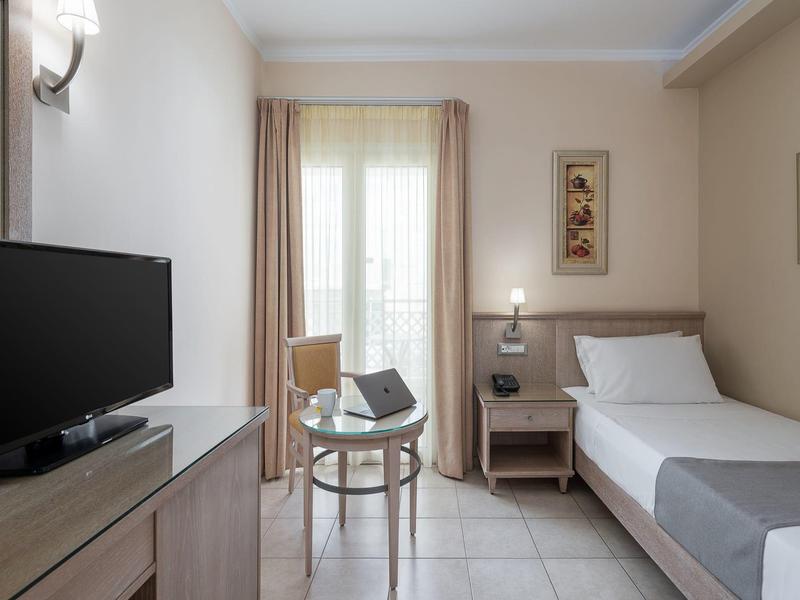 Camera d'hotel luminosa con letto singolo, scrivania, sedia e TV su mobile.