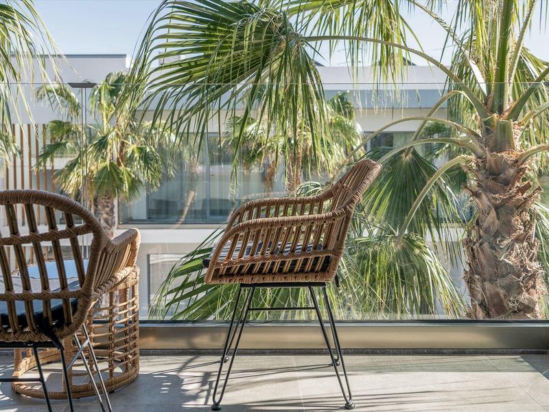 Due sedie su un balcone con ringhiera in vetro e palme sullo sfondo