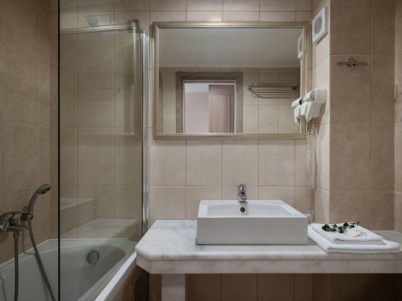 Bagno compatto con vasca, lavandino e grande specchio in tonalità neutre.