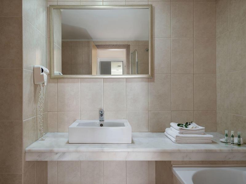 Specchio bagno moderno e luminoso dell'hotel con lavabo rettangolare e asciugamani bianchi.