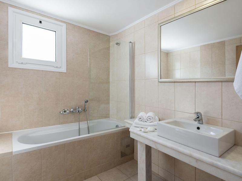 Bagno moderno con vasca, grande specchio e lavabo in tonalità neutre.