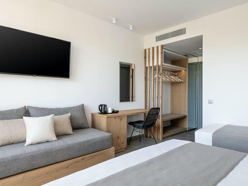 Camera d'hotel luminosa con letto matrimoniale, divano, scrivania, TV a parete e guardaroba aperto.