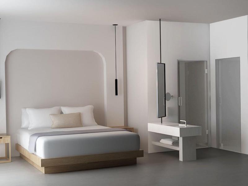 Camera d'hotel moderna con letto grande, comodino e design minimalista in tonalità neutre.