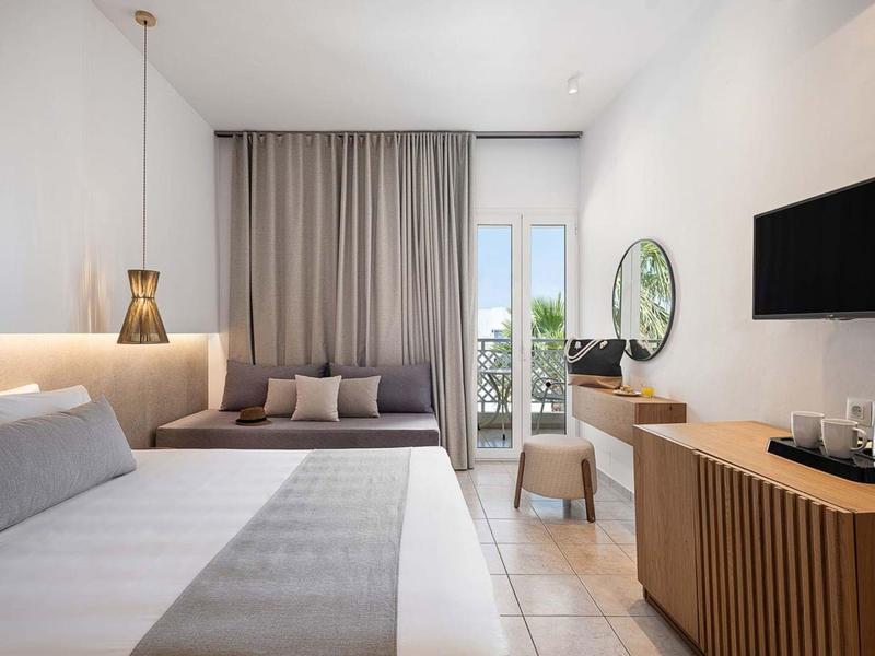 Camera d'hotel moderna con letto grande, divano, scrivania e balcone con vista esterna.