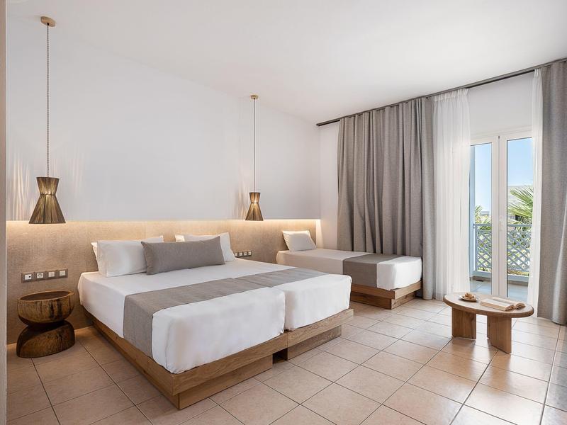 Camera d'hotel moderna con due letti singoli, tende grigie e vista dalla finestra.