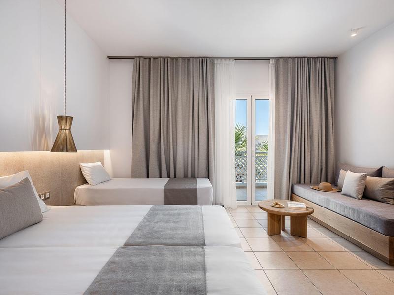 Camera d'hotel moderna con due letti, poltrone e balcone con vista sul verde.