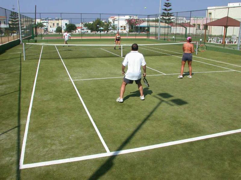 Due persone giocano a tennis su un campo verde in una giornata di sole.