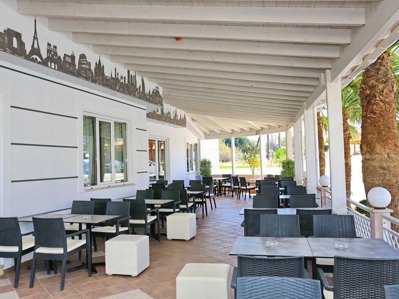 Terrazza coperta con più sedie e tavoli, palme visibili sullo sfondo.