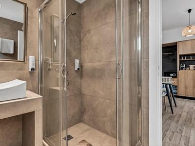 Modernes Badezimmer mit Glasdusche, Waschbecken und Zugang zu einem Wohnzimmerbereich.