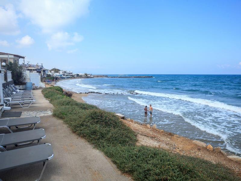 Strand mit Wellen, grasbewachsene Dünen und Liegestühle entlang eines Küstenwegs bei blauem Himmel.