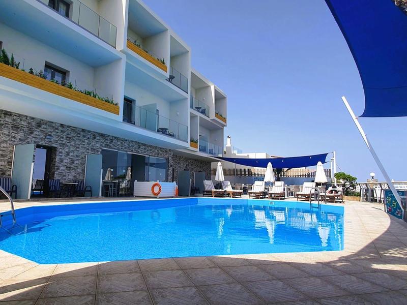 Moderner Hotelpoolbereich mit Sonnenschirmen, Sitzbereichen und Balkonen bei klarem Himmel.